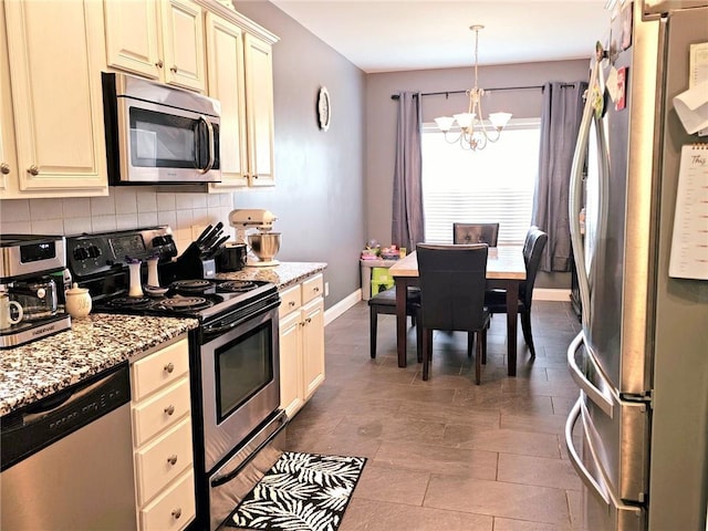 kitchen with stainless steel appliances, cream cabinetry, a chandelier, tasteful backsplash, and light stone counters