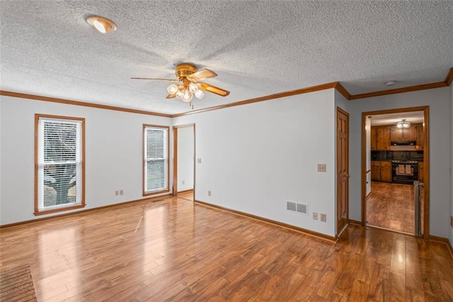 empty room featuring wood finished floors, baseboards, visible vents, ceiling fan, and ornamental molding