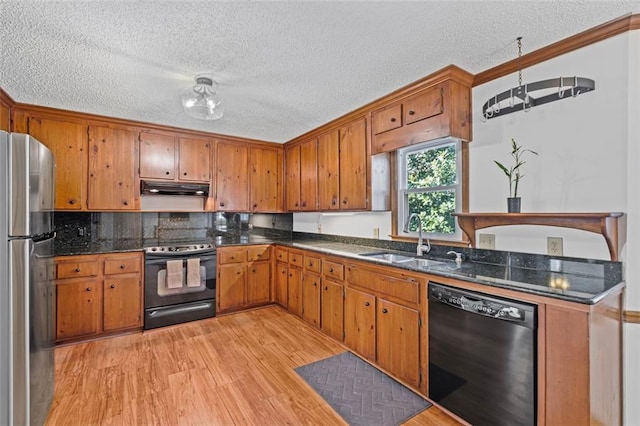 kitchen featuring black appliances, brown cabinets, under cabinet range hood, and a sink