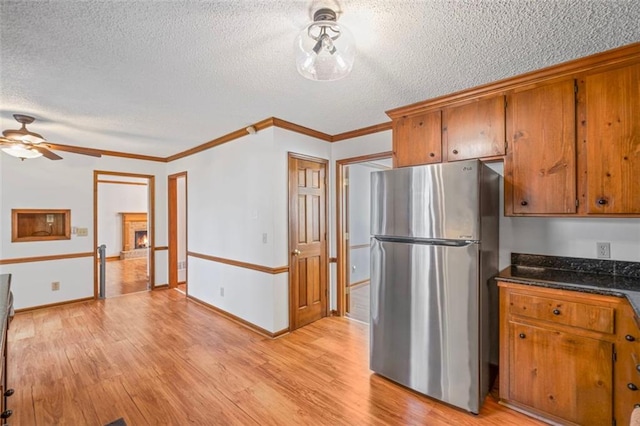 kitchen featuring dark countertops, freestanding refrigerator, light wood-style floors, a fireplace, and brown cabinetry