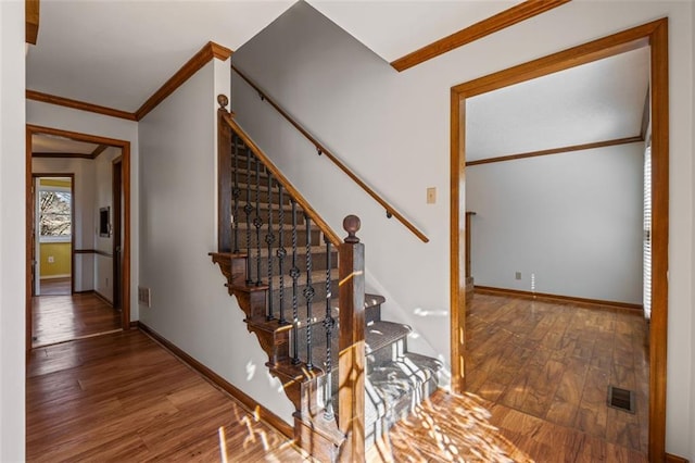 stairs featuring visible vents, wood finished floors, baseboards, and ornamental molding