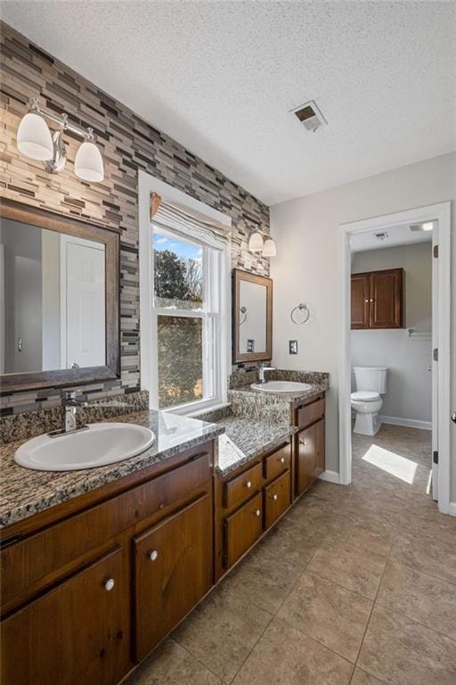 bathroom featuring double vanity, visible vents, a textured ceiling, and a sink