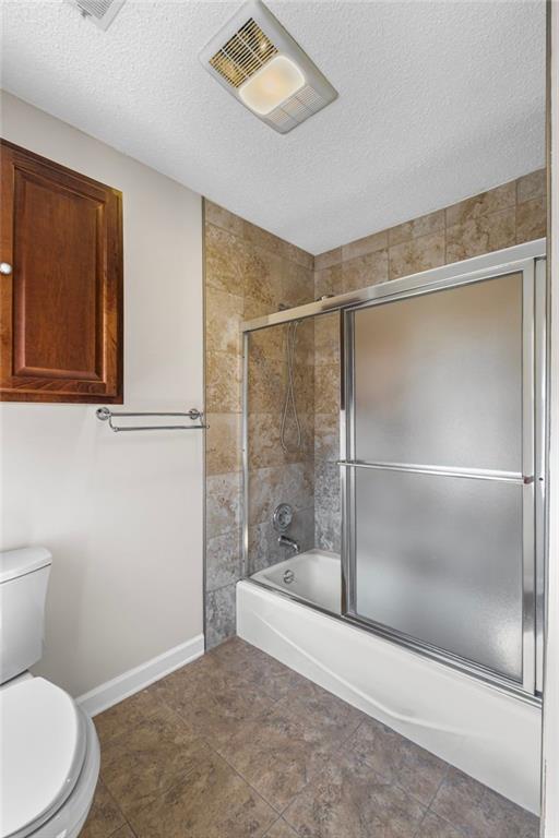 full bath featuring visible vents, enclosed tub / shower combo, toilet, and a textured ceiling