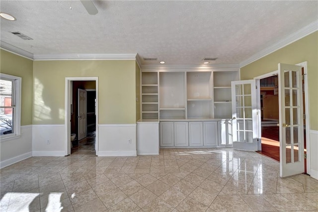 empty room with french doors, a textured ceiling, ornamental molding, and light tile floors