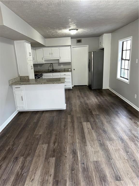 kitchen featuring a textured ceiling, white cabinets, kitchen peninsula, and stainless steel fridge