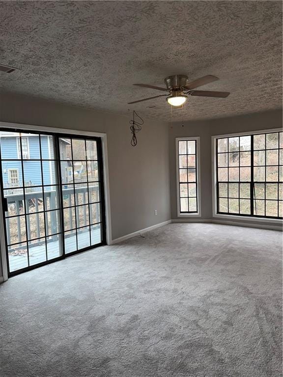 carpeted empty room with ceiling fan, plenty of natural light, and a textured ceiling