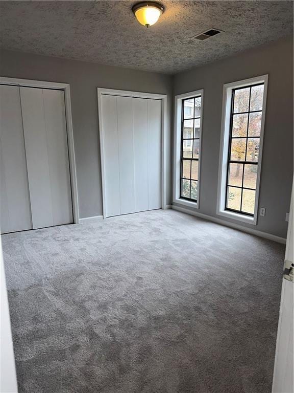 unfurnished bedroom featuring a textured ceiling, carpet flooring, and multiple closets