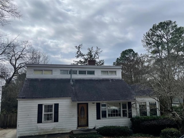 view of front of house featuring a shingled roof, a chimney, and fence