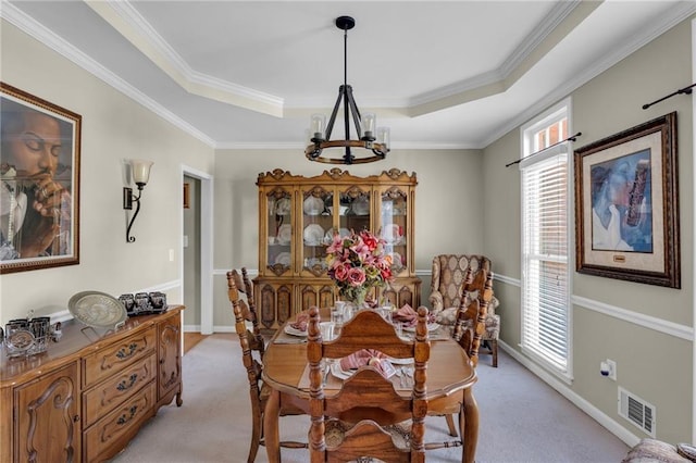 carpeted dining area with ornamental molding, a tray ceiling, and an inviting chandelier