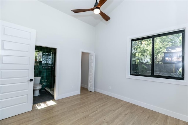 unfurnished bedroom featuring baseboards, high vaulted ceiling, ensuite bath, and light wood finished floors