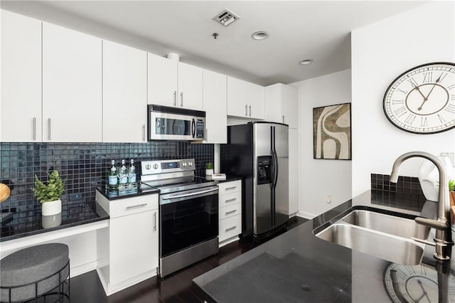 923 Peachtree St NE Unit 1238, Atlanta, GA 30309 - kitchen featuring appliances with stainless steel finishes, dark countertops, decorative backsplash, dark wood-style flooring, and white cabinetry
