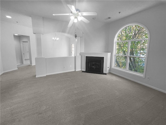 unfurnished living room featuring ceiling fan with notable chandelier, a healthy amount of sunlight, carpet floors, and vaulted ceiling