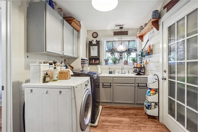 laundry area featuring cabinets, light wood-type flooring, sink, an inviting chandelier, and washing machine and clothes dryer