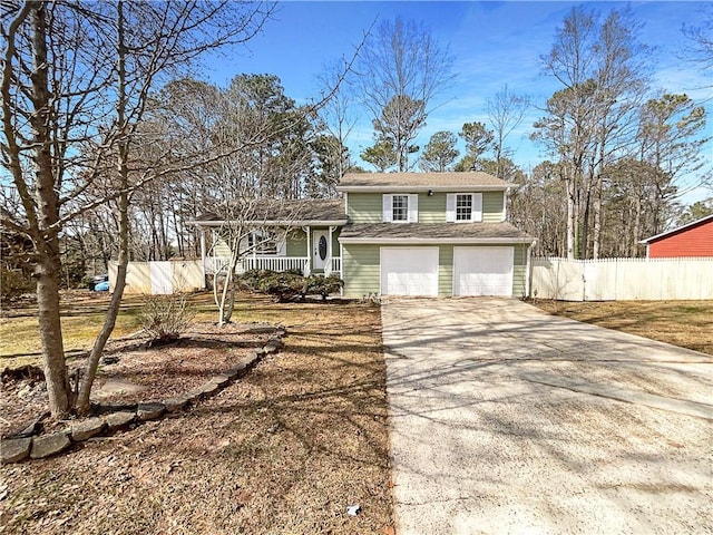 split level home featuring concrete driveway, covered porch, fence, and an attached garage