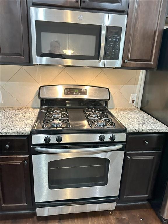 kitchen featuring appliances with stainless steel finishes, dark hardwood / wood-style flooring, backsplash, and light stone counters