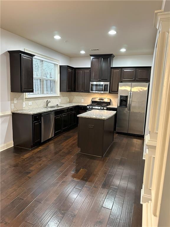 kitchen featuring appliances with stainless steel finishes, tasteful backsplash, dark hardwood / wood-style flooring, light stone counters, and a center island