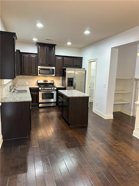 kitchen featuring stainless steel appliances, dark wood-type flooring, a kitchen island, light stone counters, and sink