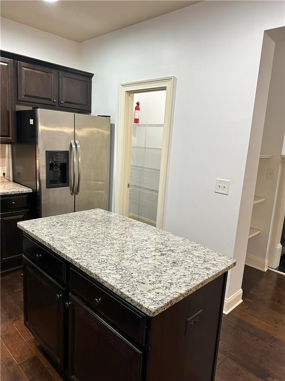 kitchen featuring stainless steel refrigerator with ice dispenser, light stone counters, dark hardwood / wood-style floors, and a kitchen island