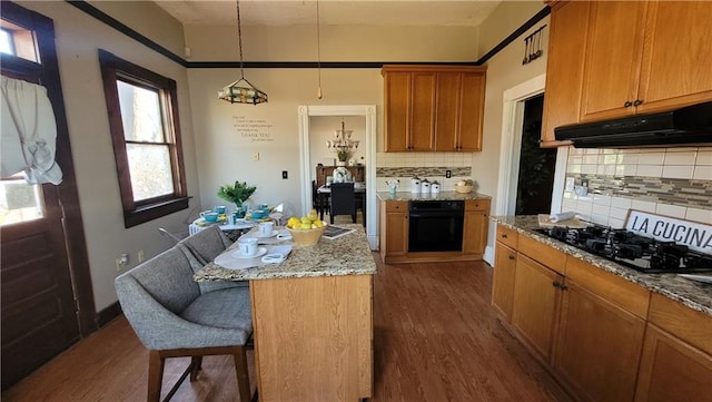 kitchen featuring dark wood finished floors, under cabinet range hood, light stone counters, black appliances, and a kitchen breakfast bar