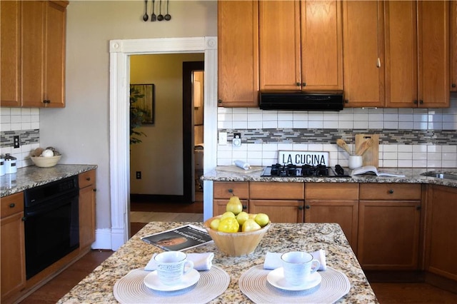 kitchen with decorative backsplash, light stone countertops, brown cabinets, ventilation hood, and black appliances