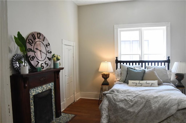 bedroom with a fireplace with flush hearth, baseboards, and dark wood-type flooring