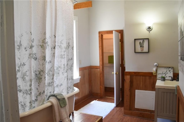 full bath featuring a wainscoted wall, wooden walls, wood finished floors, vanity, and a freestanding bath