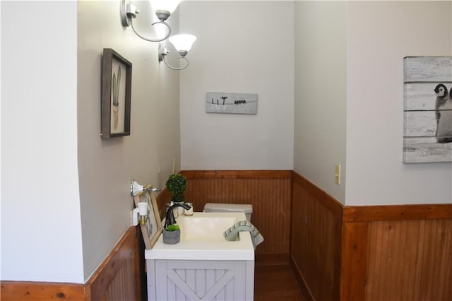 half bath with a wainscoted wall, toilet, wood walls, and vanity