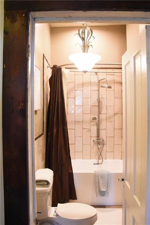 bathroom featuring toilet and shower / bath combination with curtain