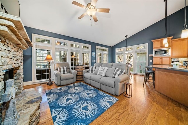 living room with ceiling fan, a stone fireplace, light wood-type flooring, and a wealth of natural light