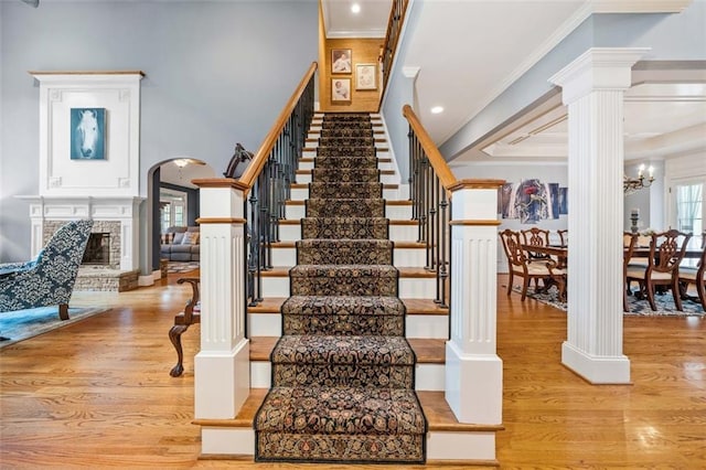 staircase with a notable chandelier, decorative columns, hardwood / wood-style flooring, a fireplace, and ornamental molding