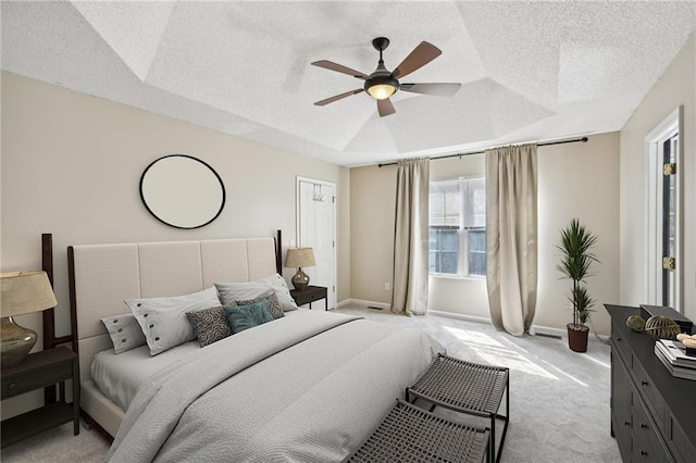 bedroom with a tray ceiling, light carpet, a textured ceiling, and baseboards