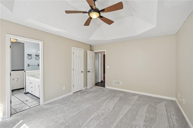 unfurnished bedroom with baseboards, ensuite bathroom, a textured ceiling, a raised ceiling, and light carpet