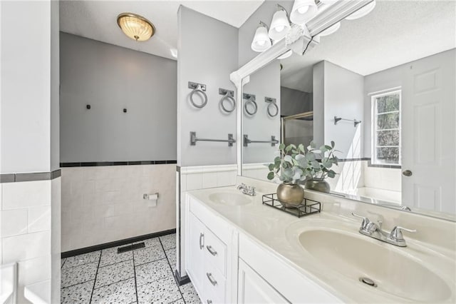 full bathroom with tile walls, a stall shower, wainscoting, and a sink