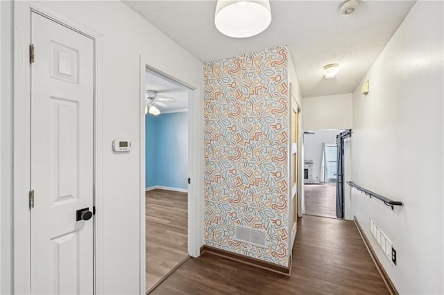 hallway with visible vents, a textured ceiling, baseboards, and wood finished floors