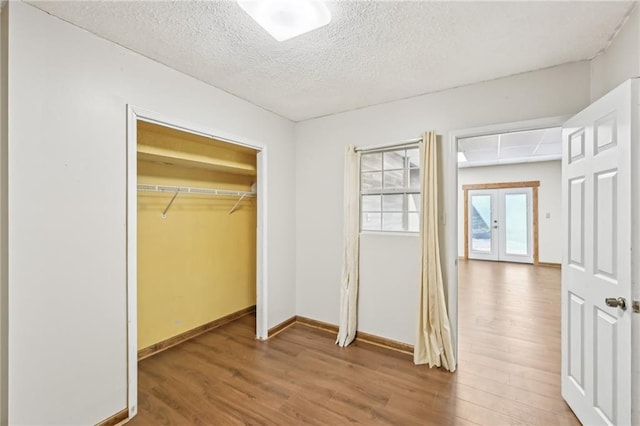 unfurnished bedroom featuring a textured ceiling, wood finished floors, french doors, a closet, and baseboards