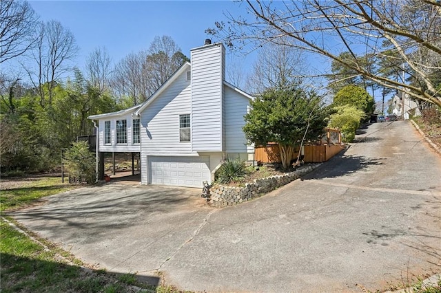 view of side of property featuring driveway, a chimney, and a garage