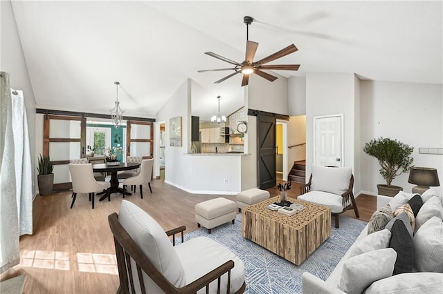 living area with ceiling fan with notable chandelier, lofted ceiling, wood finished floors, and baseboards