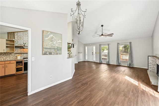 unfurnished living room featuring lofted ceiling, ceiling fan with notable chandelier, dark wood-style floors, a stone fireplace, and baseboards