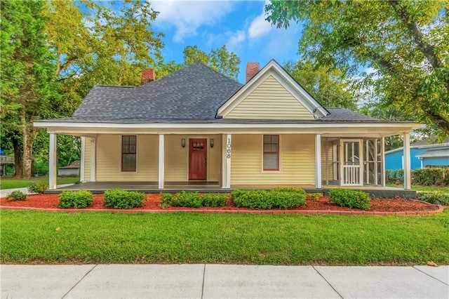 farmhouse-style home with covered porch, a chimney, and a front lawn