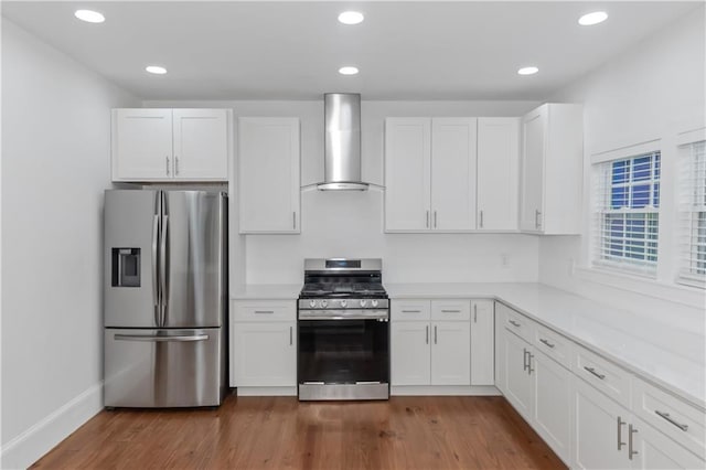 kitchen featuring stainless steel appliances, wood finished floors, white cabinetry, light countertops, and wall chimney range hood