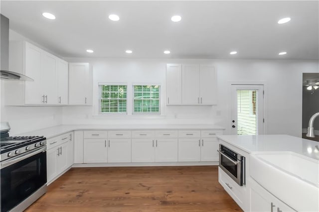 kitchen with stainless steel appliances, recessed lighting, light countertops, white cabinets, and wall chimney range hood