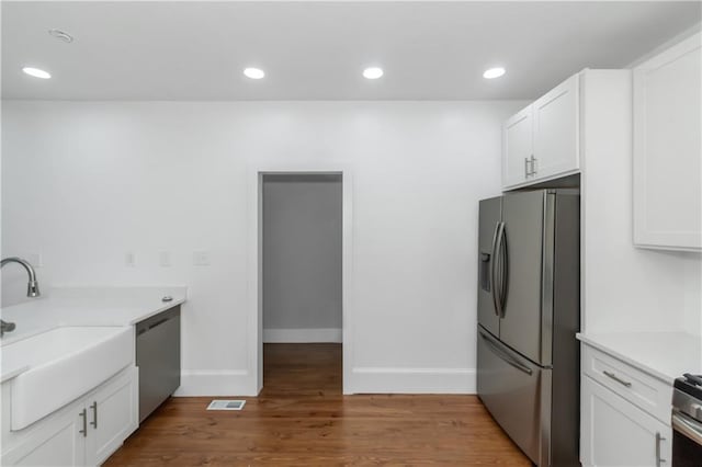 kitchen with visible vents, appliances with stainless steel finishes, white cabinets, a sink, and wood finished floors