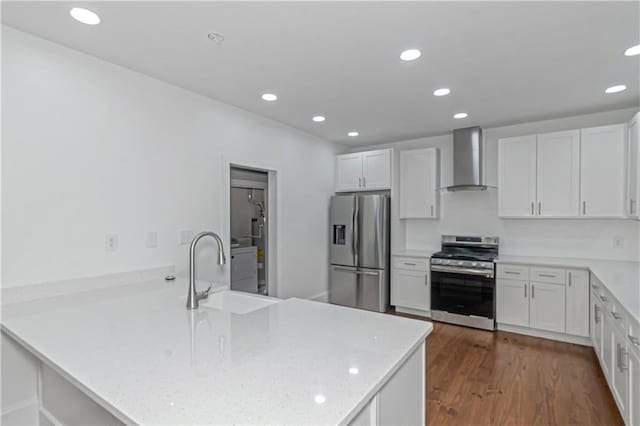 kitchen with dark wood-style flooring, stainless steel appliances, a sink, a peninsula, and wall chimney exhaust hood