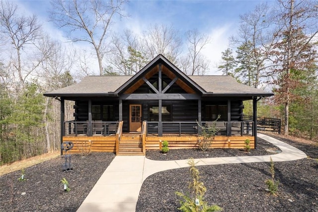 cabin featuring log siding, covered porch, and roof with shingles