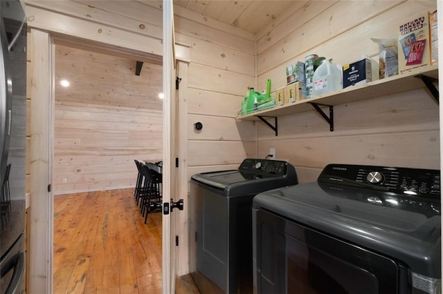 clothes washing area with laundry area, wooden walls, light wood-style flooring, and washing machine and clothes dryer