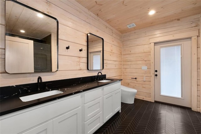 bathroom with double vanity, wooden walls, toilet, and a sink