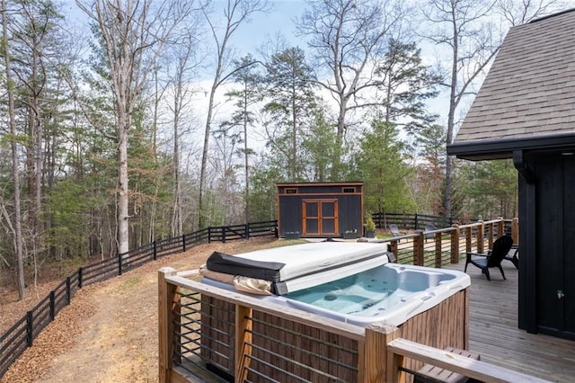 wooden terrace featuring a fenced backyard, an outbuilding, a storage shed, and a hot tub