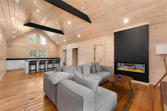 living room featuring a large fireplace, wood walls, light wood-type flooring, beam ceiling, and wooden ceiling