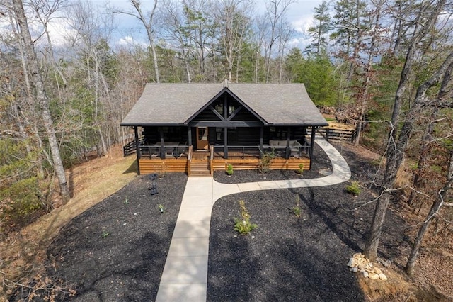 view of front facade with a view of trees, roof with shingles, covered porch, and driveway