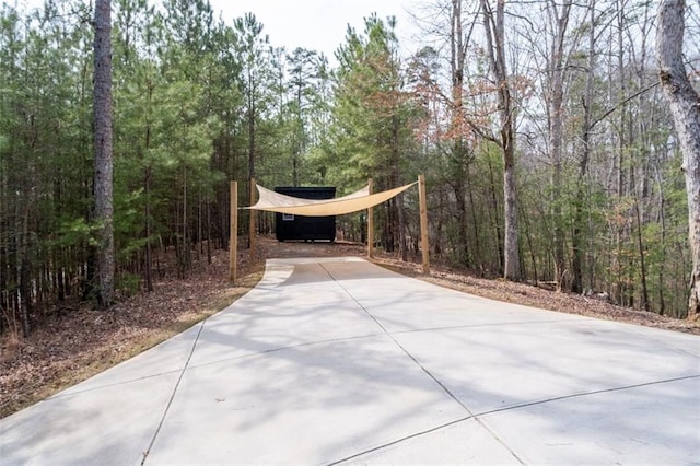 exterior space featuring a carport, concrete driveway, and a forest view